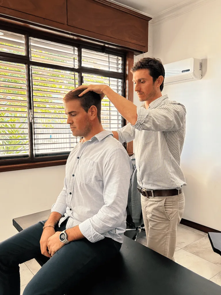 Fisioterapeuta evaluando el cuello de un paciente sentado en la clínica