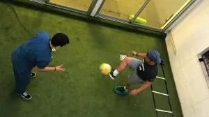 Fisioterapeuta y paciente en un ejercicio de agilidad con pelota sobre césped sintético