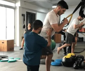 Fisioterapeuta asistiendo a un paciente en un ejercicio con TRX en el gimnasio
