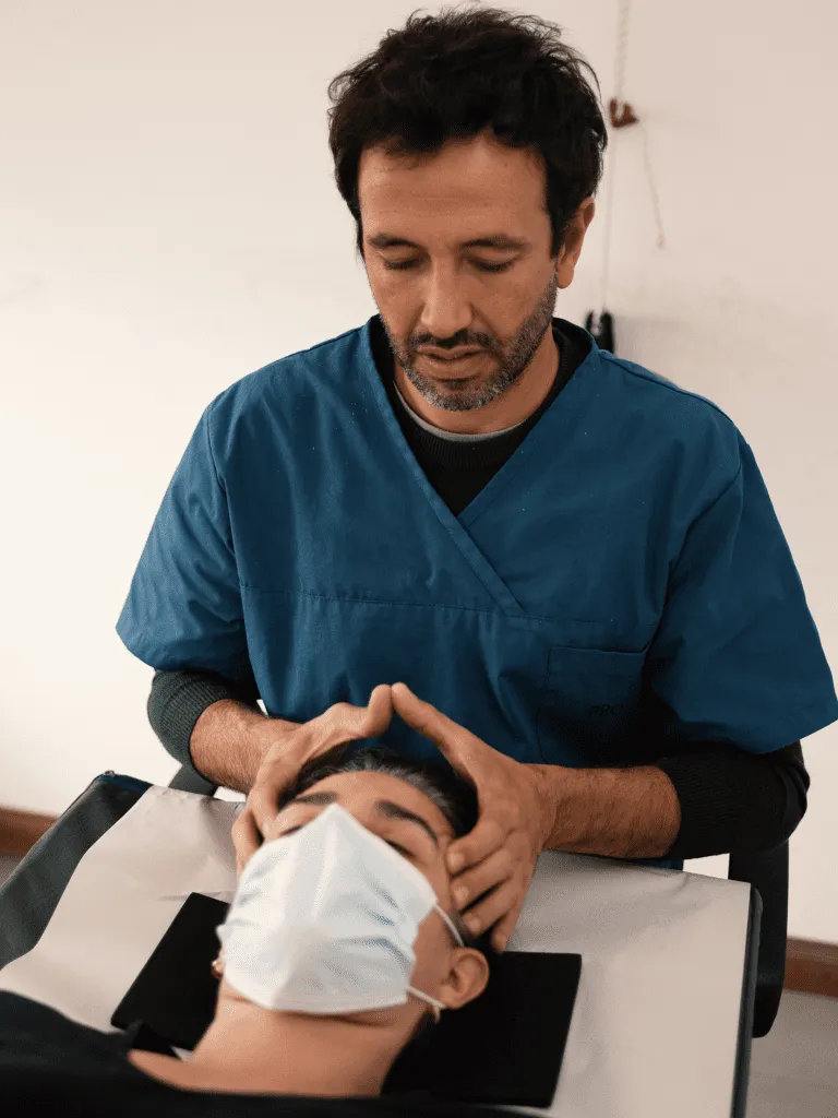 Fisioterapeuta con uniforme azul realizando una maniobra manual en el cuello de un paciente con mascarilla