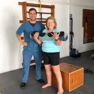 Fisioterapeuta con uniforme azul y una paciente sosteniendo un rodillo en la clínica