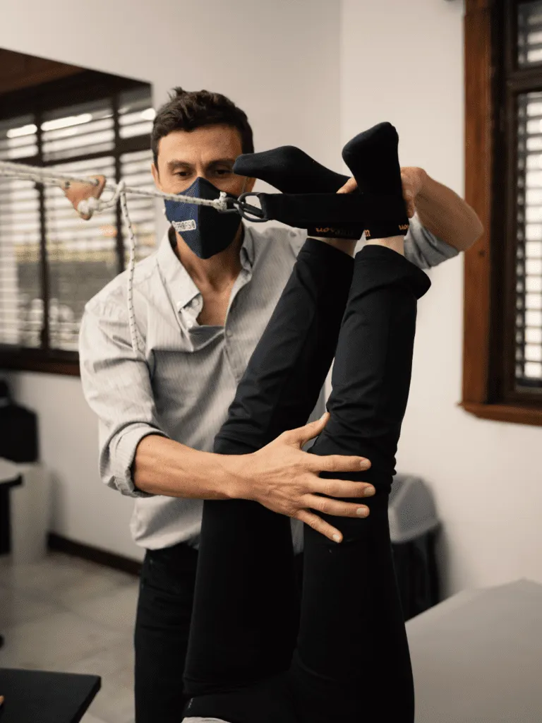 Fisioterapeuta con mascarilla elevando las piernas de un paciente en una sesión de reeducación postural