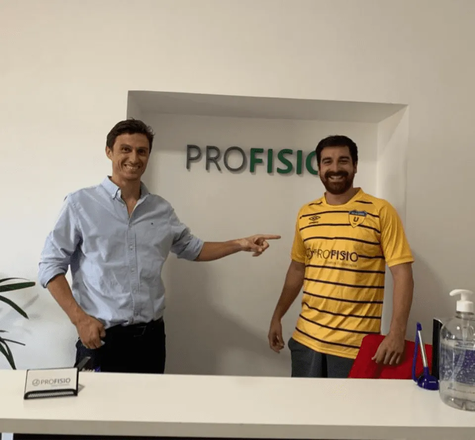 Dos personas posando frente al cartel de Profisio en la recepción