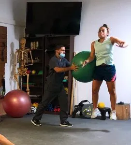 Paciente realizando un ejercicio con pelota de ejercicio asistida por un profesional en la clínica