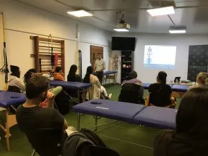 Clase o charla con asistentes sentados en camillas en una sala de la clínica