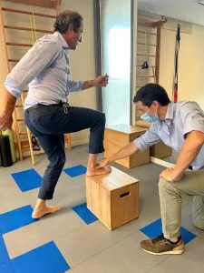 Fisioterapeuta evaluando el apoyo del pie de un paciente que sube a un cajón de madera