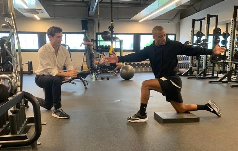 Dos hombres realizando ejercicios de estiramiento y fuerza en un gimnasio