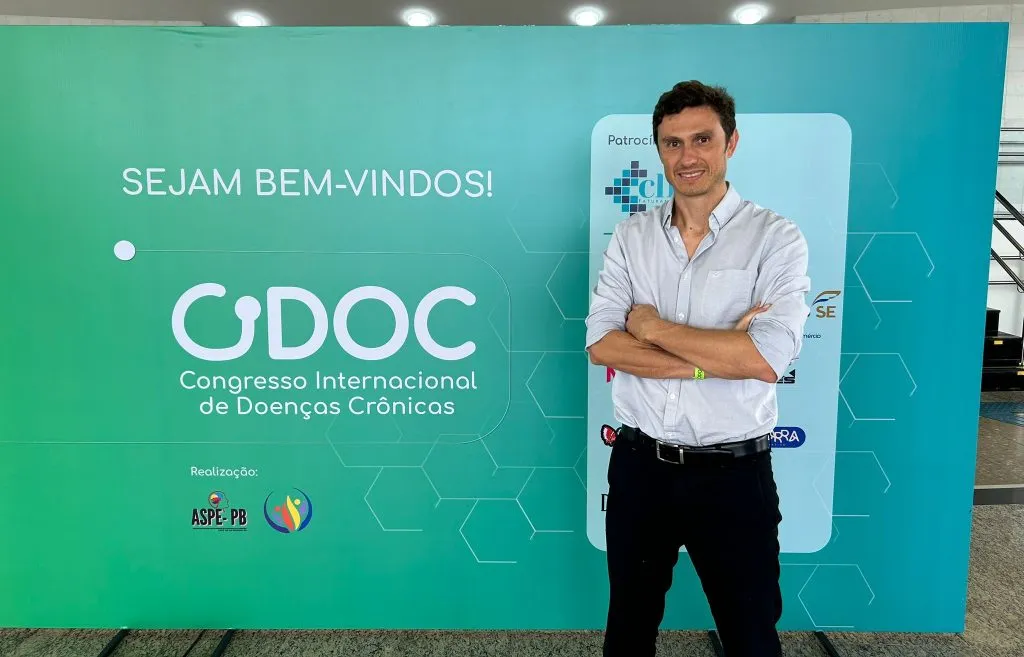 Profesional frente al cartel del Congresso Internacional de Doenças Crônicas