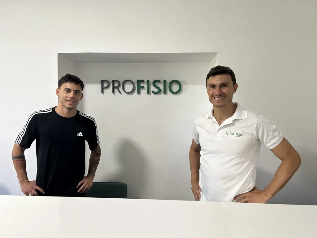 Dos profesionales posando frente al cartel de Profisio