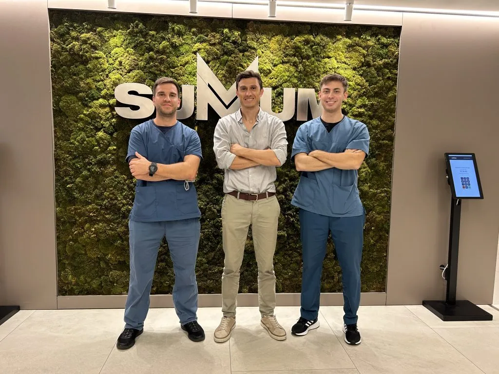 Tres profesionales posando frente al cartel de Summum en la Clínica del Lago